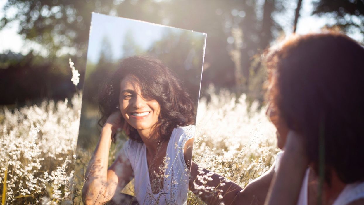 A beautiful brunette woman sits in a field as she looks into a mirror
