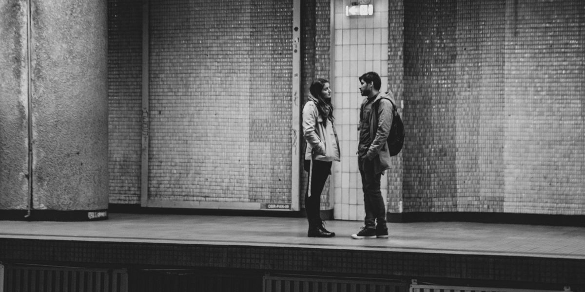 A black and white photo of a couple (guy and girl) in a tense conversation while standing on a train platform.