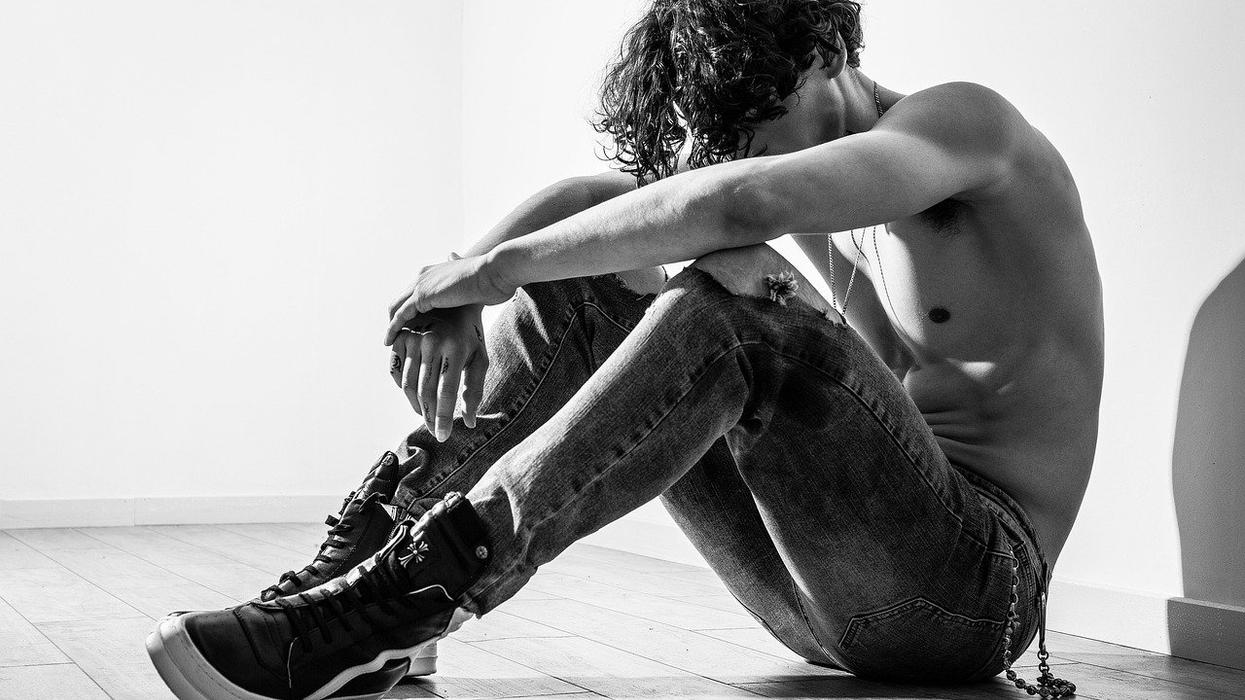 A black and white photo of a fit young man, hunched over, shirtless and sitting on the floor