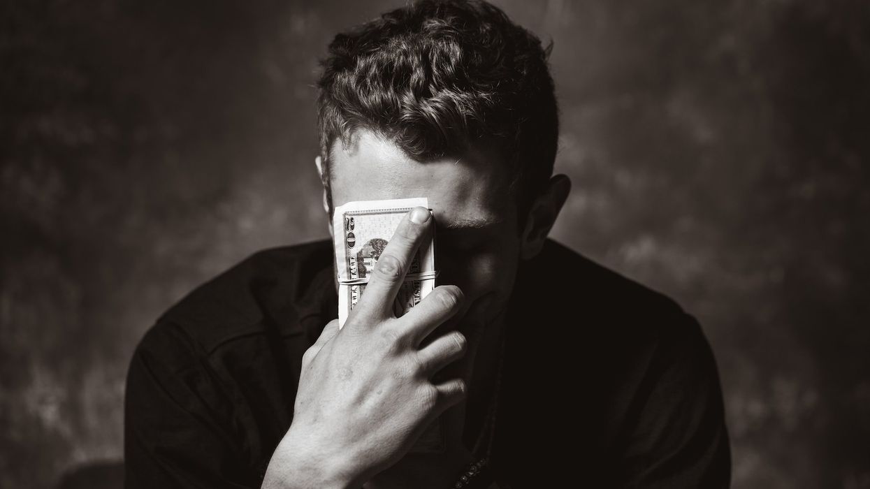 A black and white photo of a seemingly distressed man holding a stack of 20s to his forehead