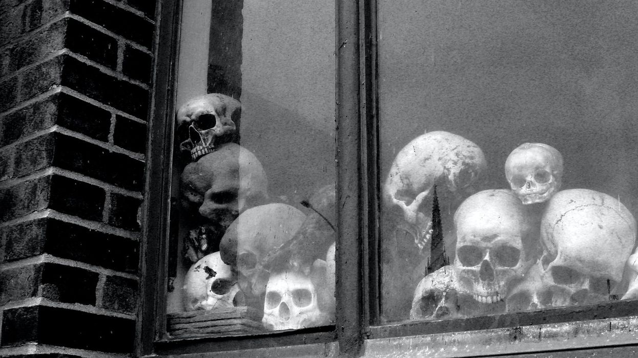 A black and white photo of a window, on the inside there are a pile of skulls
