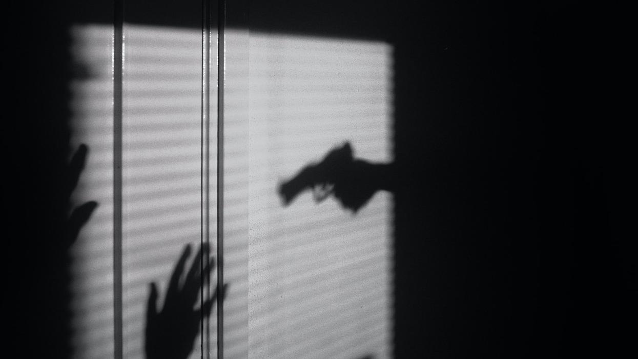A black and white photo, of the shadow of a gun barring down on someone surrendering