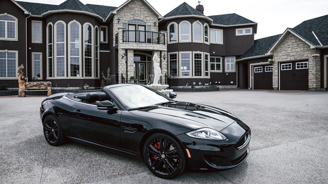 A black convertible car parked outside a mansion