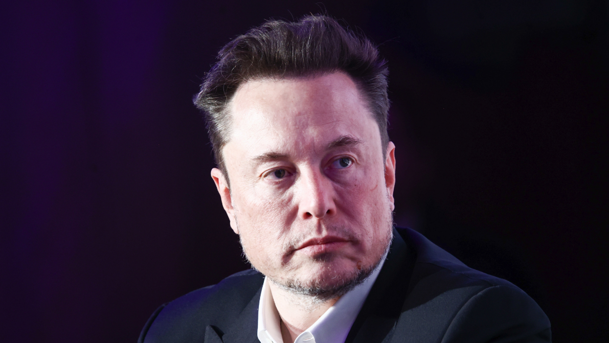 A closeup shot of Elon Musk's face. He is looking off toward the right of the frame with a slight frown.