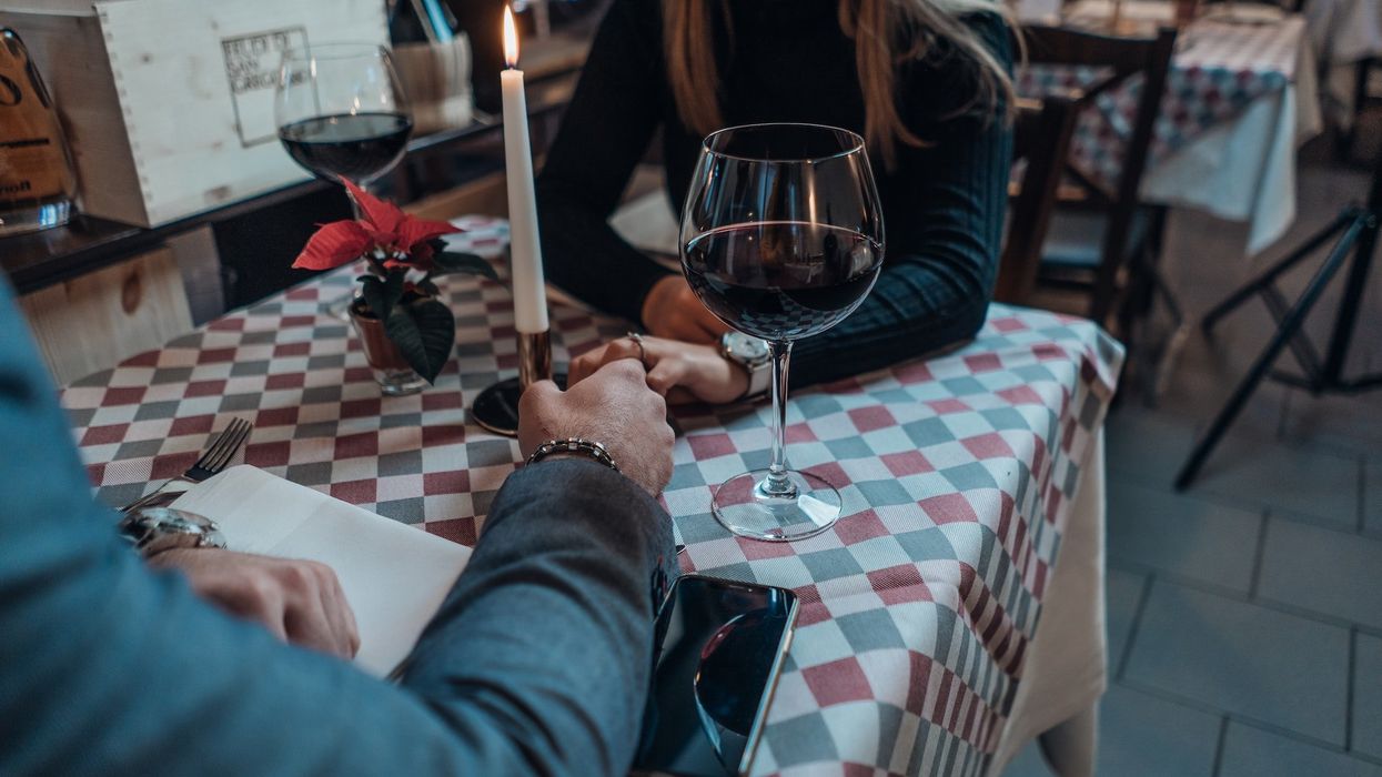 A couple holds hands on a date, candlelit table and two glasses of red wine