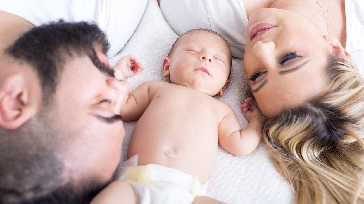 A couple lies in bed with a baby between them
