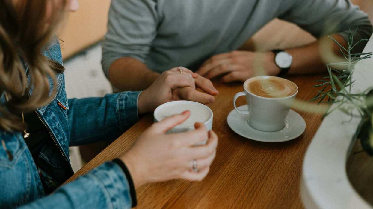 A couple sits at a cafe, drinks cappuccinos and hold hands.