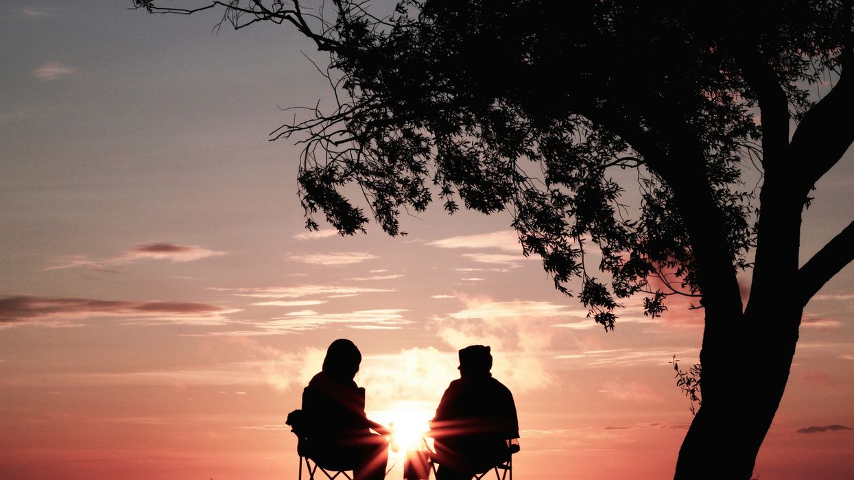 A couple sitting in profile in front of a sunset.