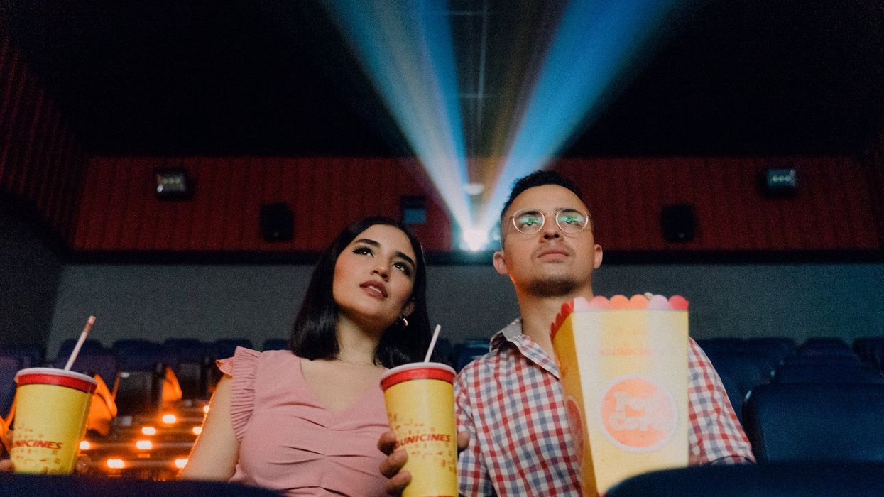 A couple watch a movie, in a theater, holding popcorn and two drinks