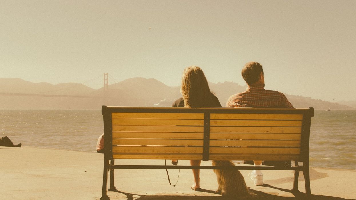 A couple with their backs to the camera sits on a bench looking out thinking