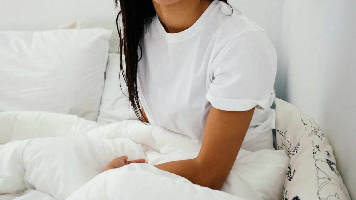 A faceless woman sits in a bed, wearing only a white t-shirt.