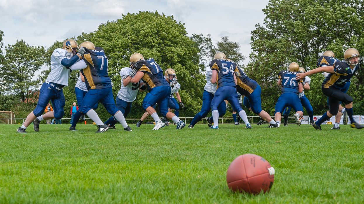 A football on the ground with players scuffling in the background