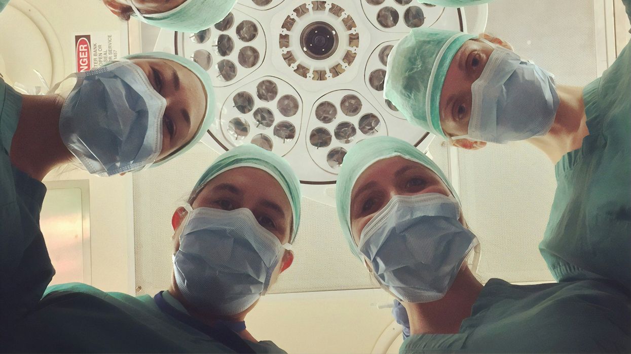 A group of masked surgeons look down over a patient.