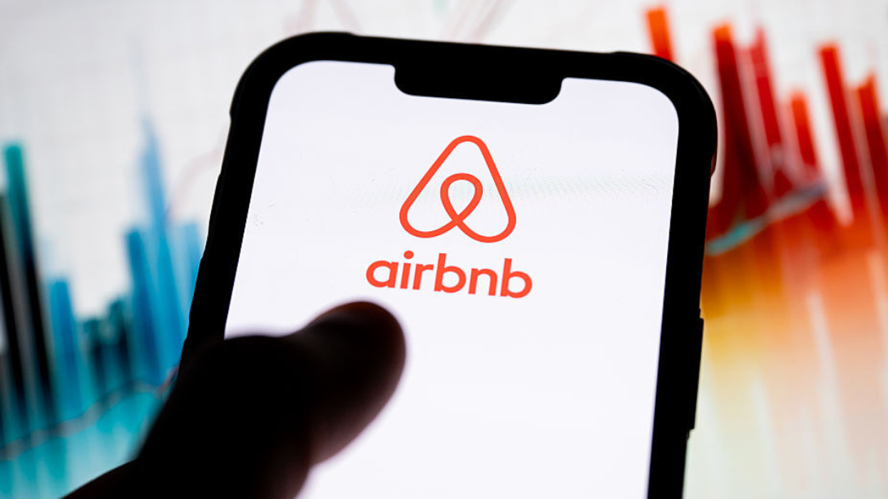 A hand holding a phone displaying the Airbnb Logo