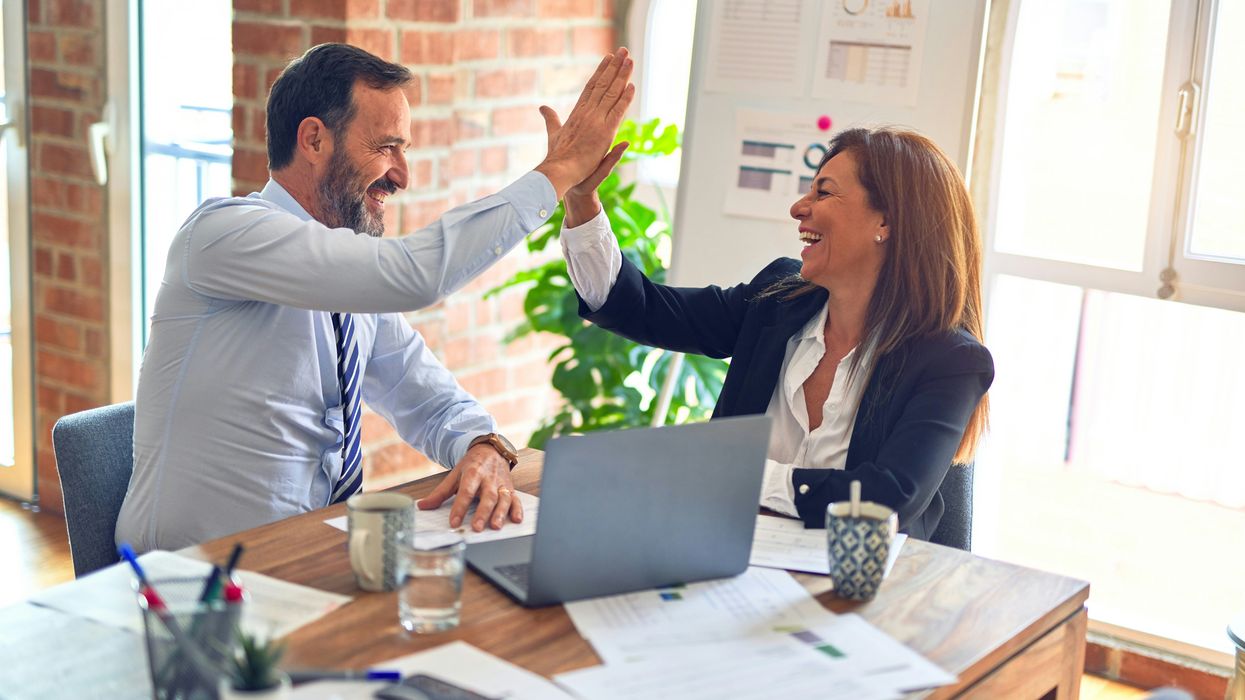 A man and a woman in an office, giving each other a high five.