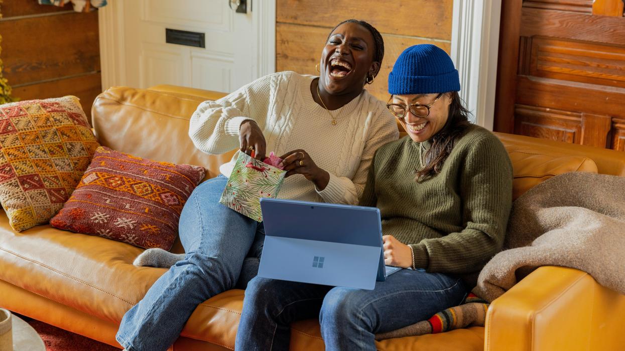 a man and a woman sitting on sofa and laughing at something on a laptop