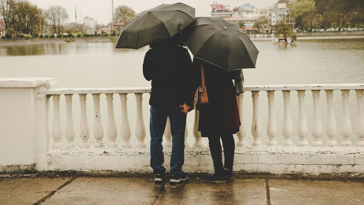 A man and a woman under umbrellas looking our over a bridge.