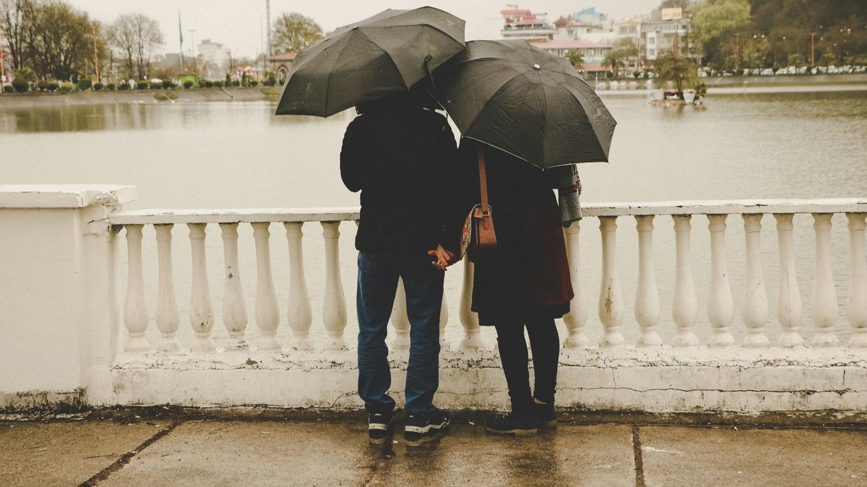 A man and a woman under umbrellas looking our over a bridge.