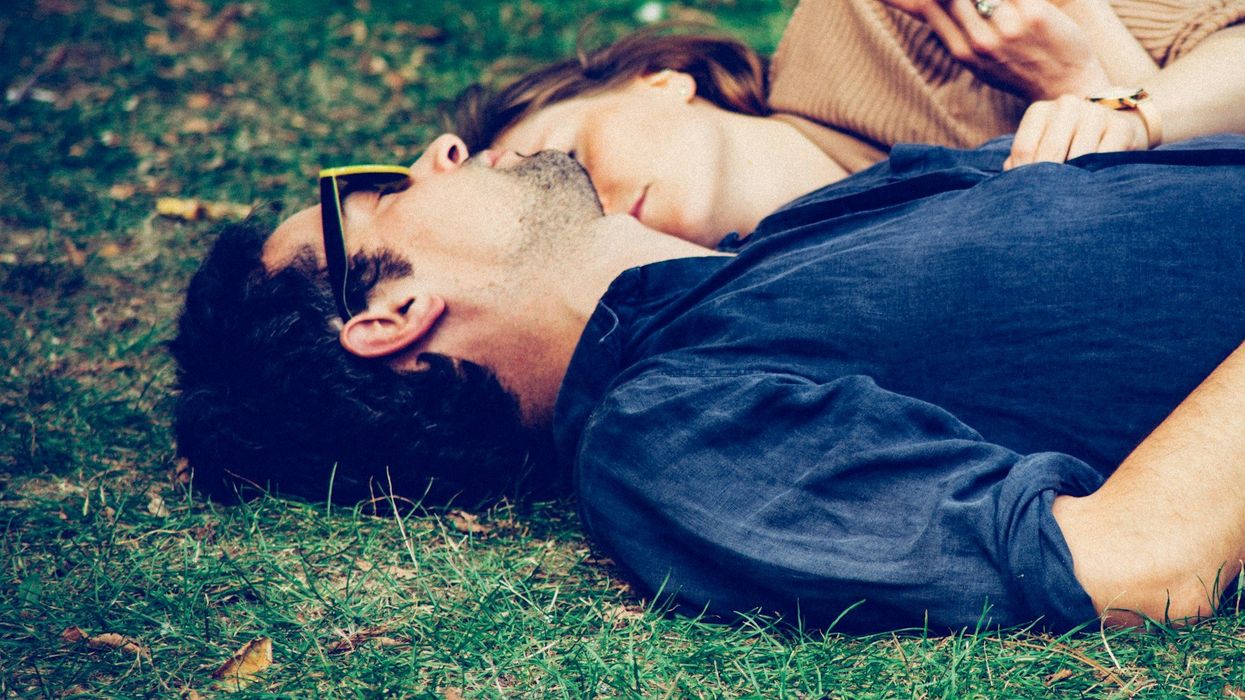 A man and woman lay on the grass cuddling and napping.