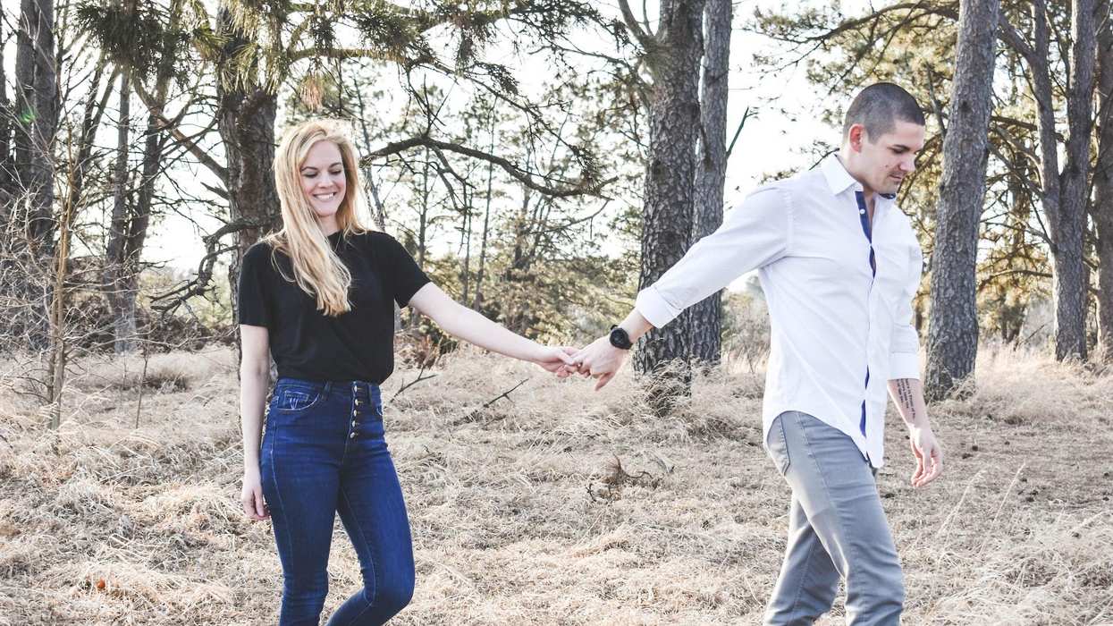 A man and woman walk through the woods holding hands