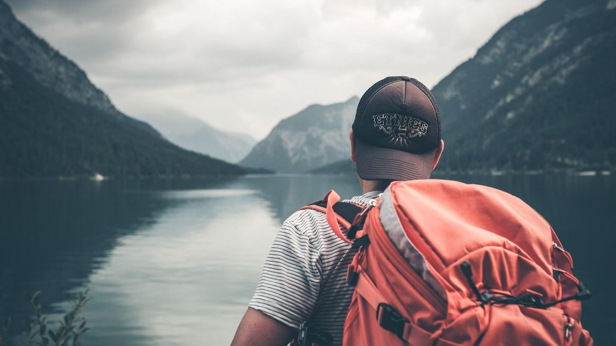 A man backpacking on river, heading towards mountains