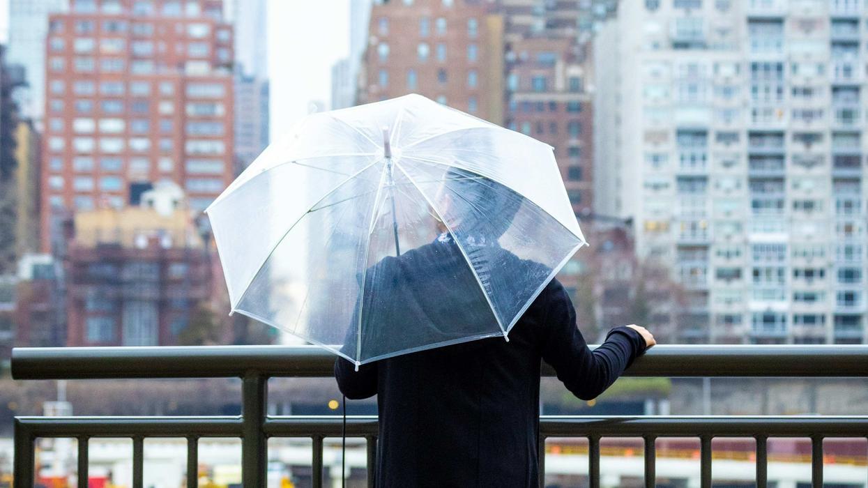 A man holding a transparent umbrella on a boardwalk in a city