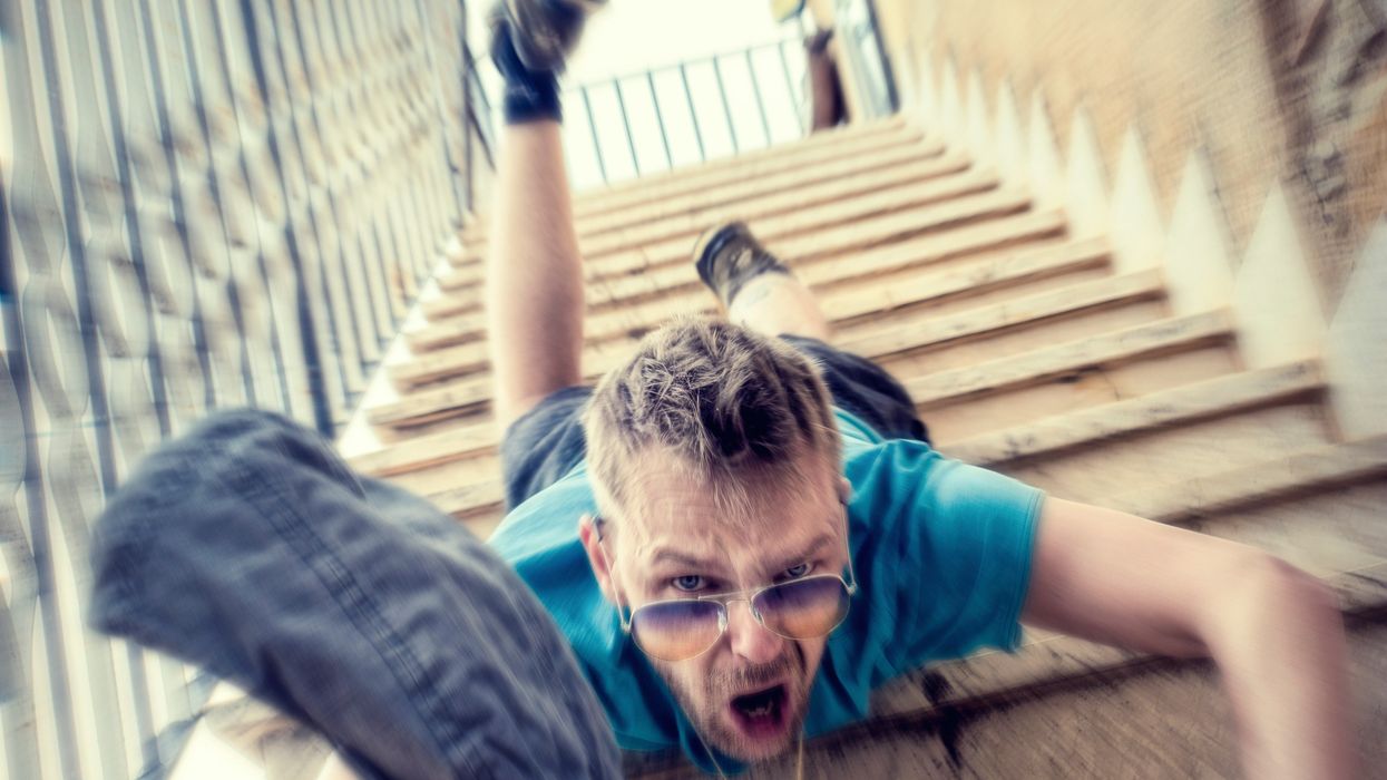 A man in a blue shirt and shorts falling head first down concrete stairs