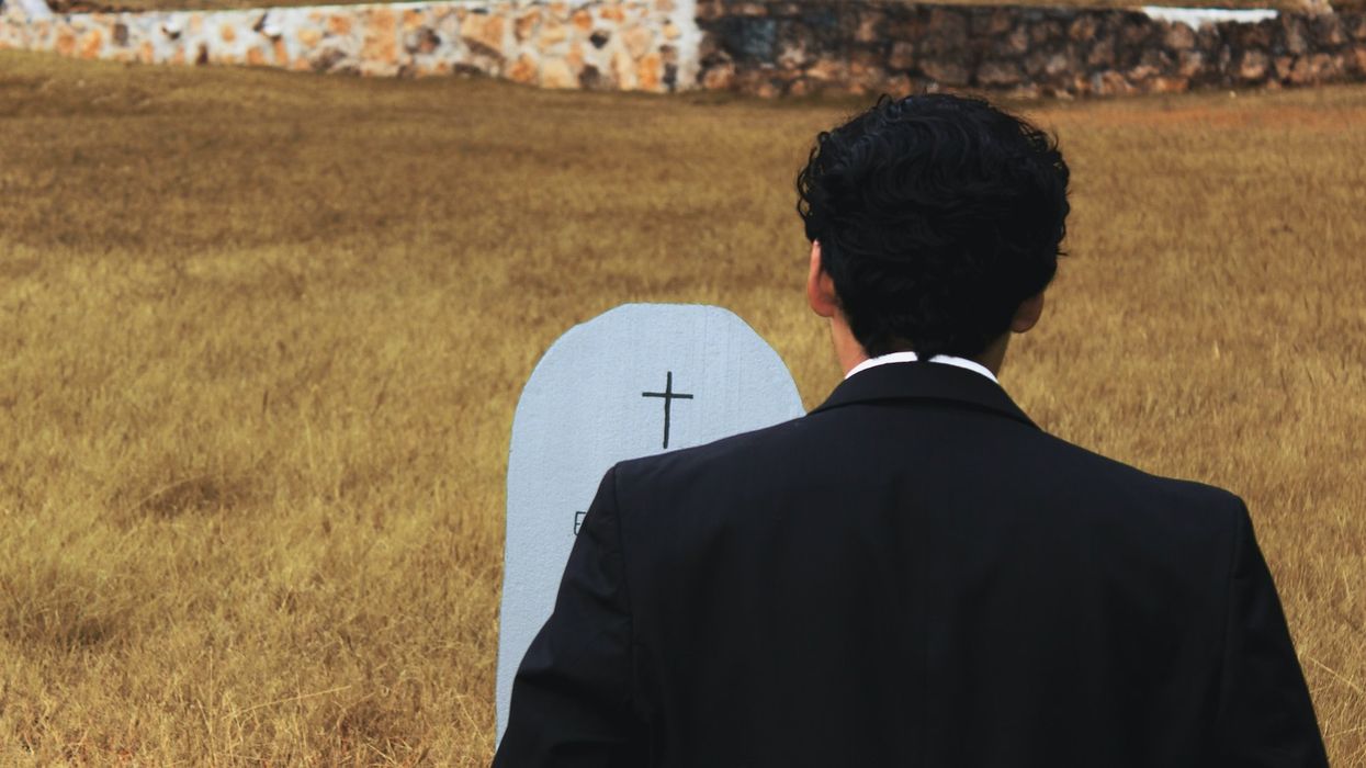 A man in a tux stands in front of a grave in a field of grass