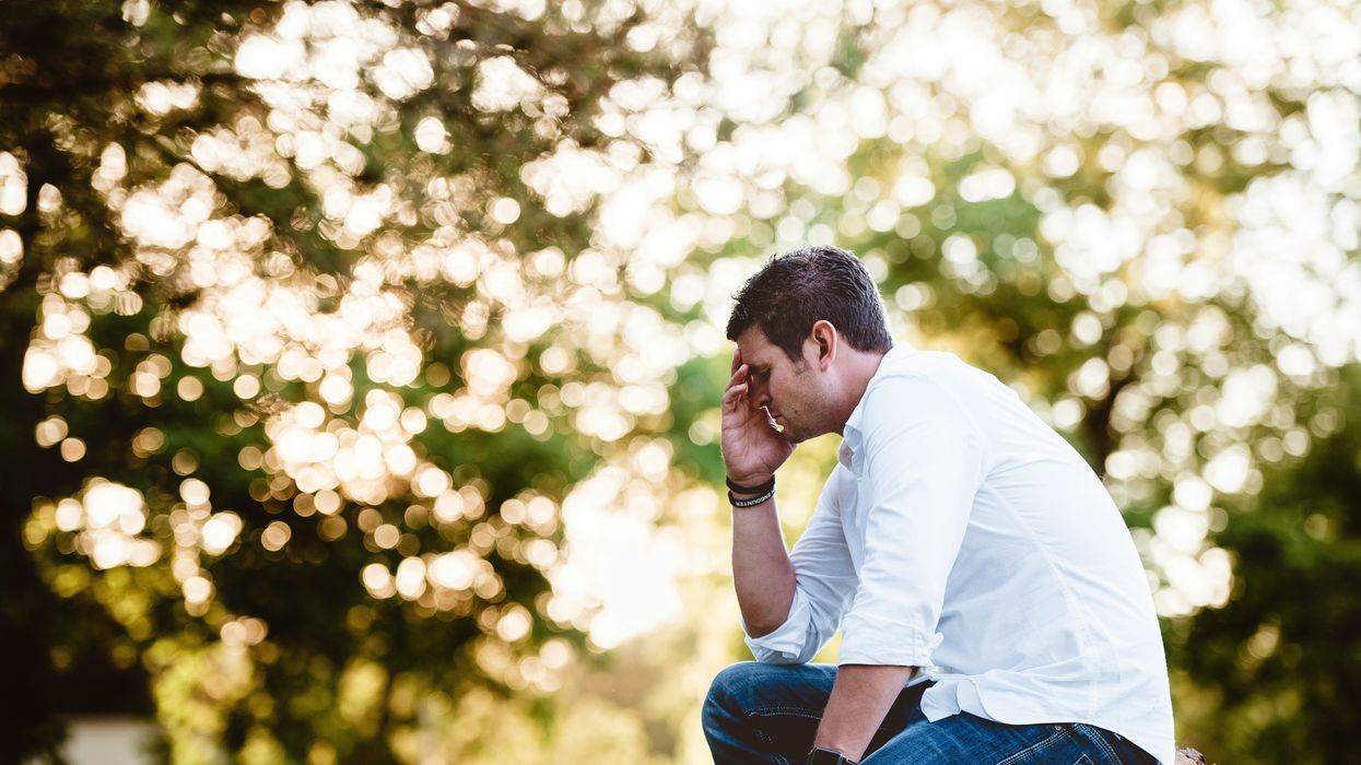 A man kneeling down with his head in his hands.