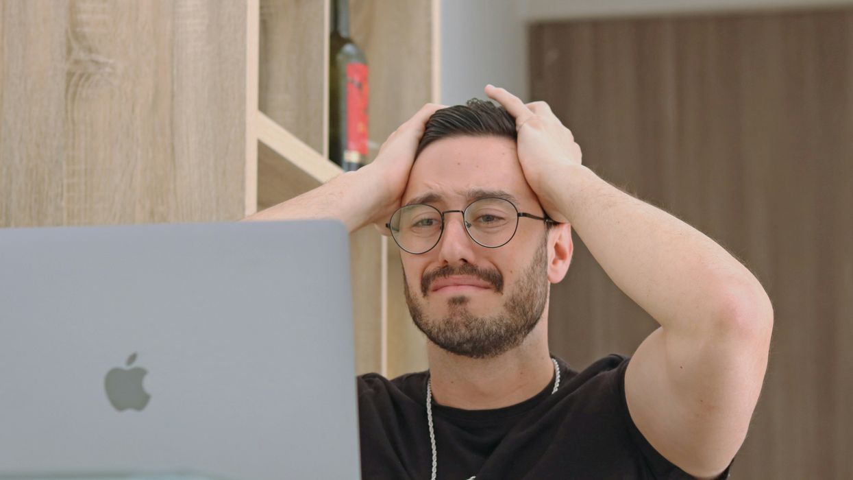 A man looking at a computer with his hands on his head.