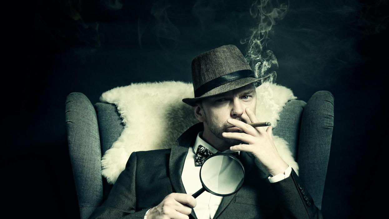 A man sits in a chair with a magnifying glass while smoking a cigarette