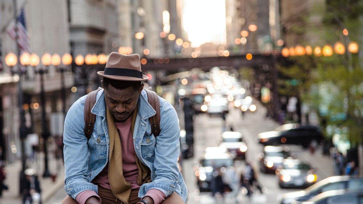 A man sits with a forlorn look while the blurry city bustles behind him