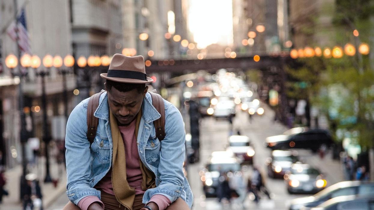 A man sits with a forlorn look while the blurry city bustles behind him