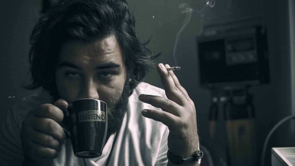A man smoking a cigarette and drinking a cup of coffee