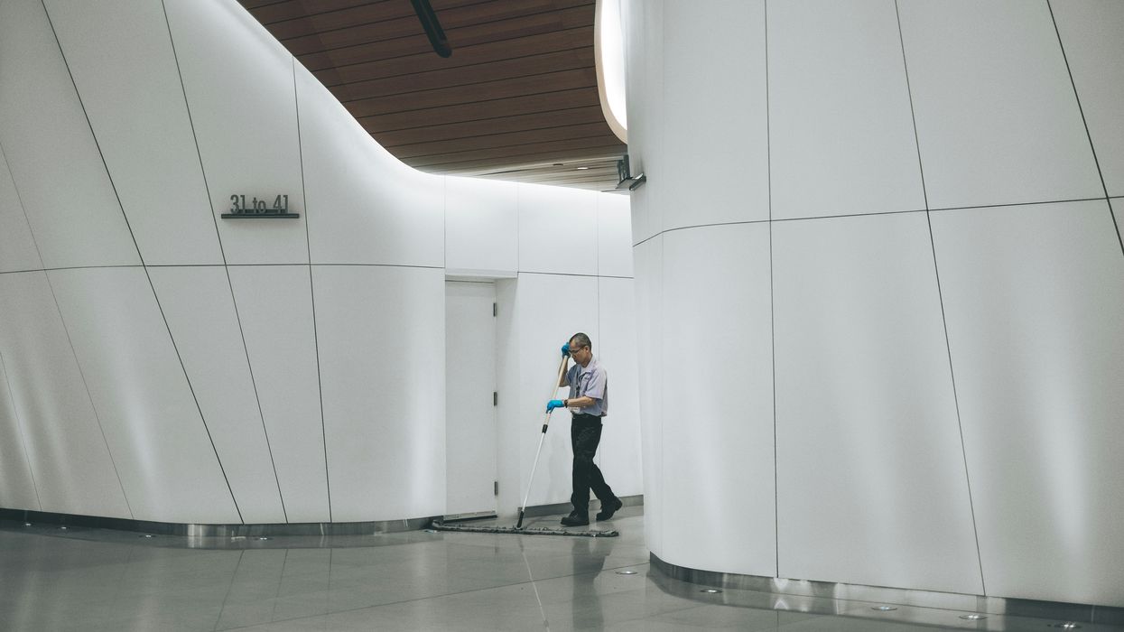 A man sweeping the floor in an empty hall.