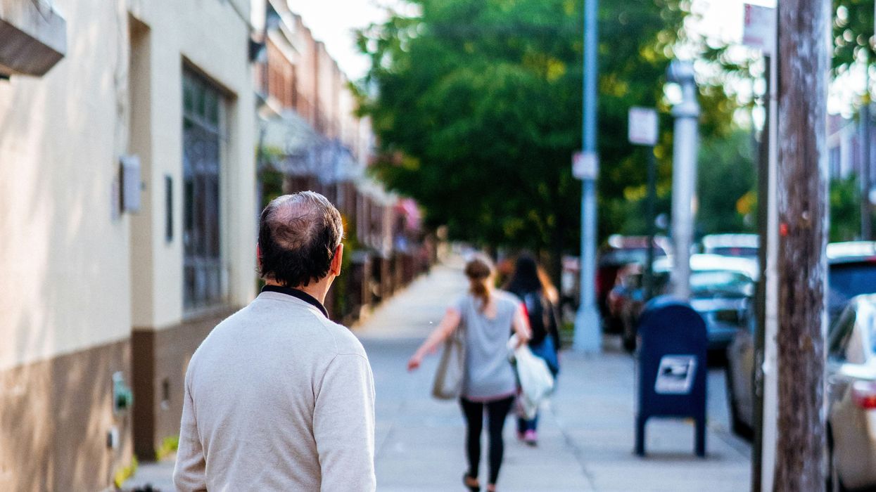 A man watching a woman walk away on the sidewalk