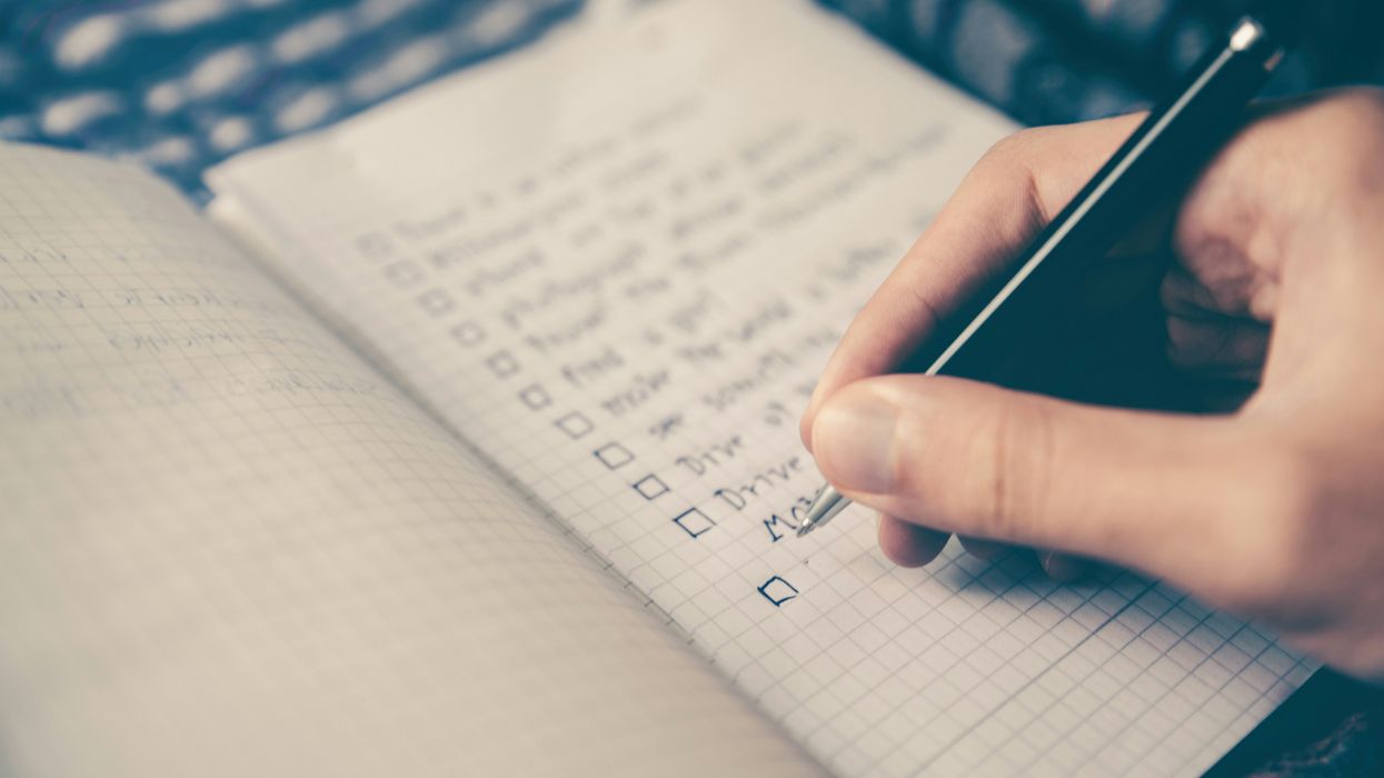 A man writing a check list in a grid notebook.
