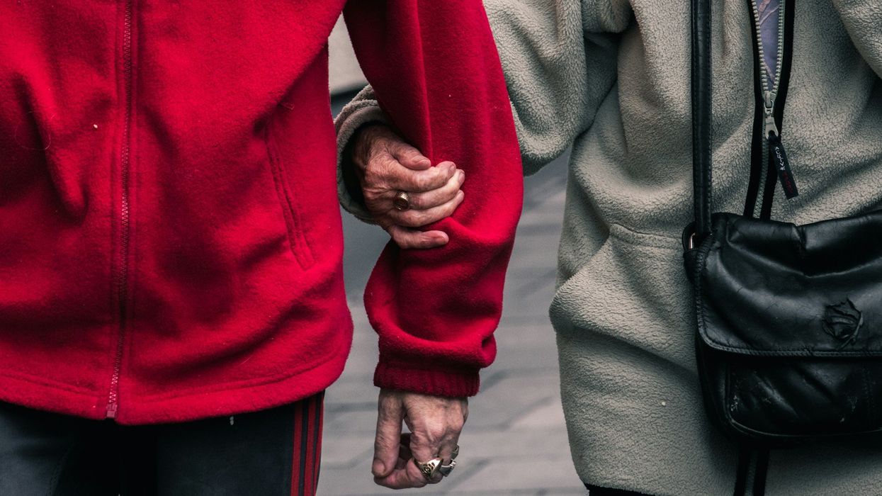 A mid-shot of an unidentifiable, older couple walking in the street. The wife's hand holds her husband's arm.