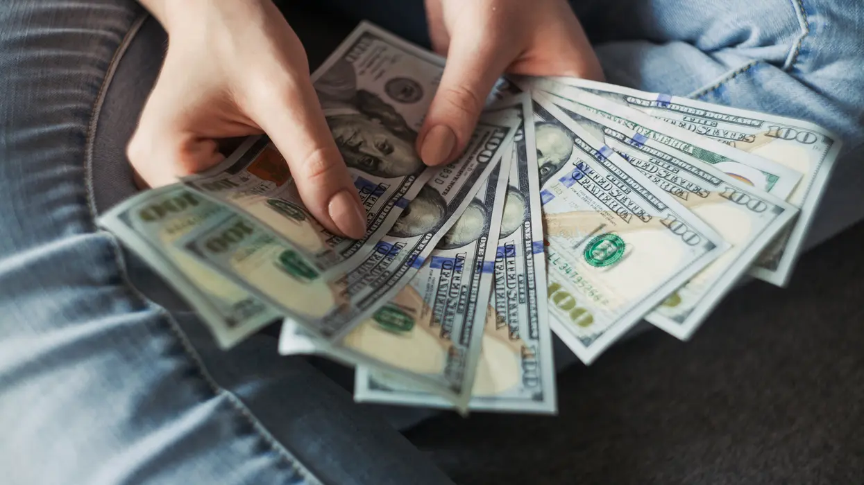 A pair of hands holding a fan of $100 bills