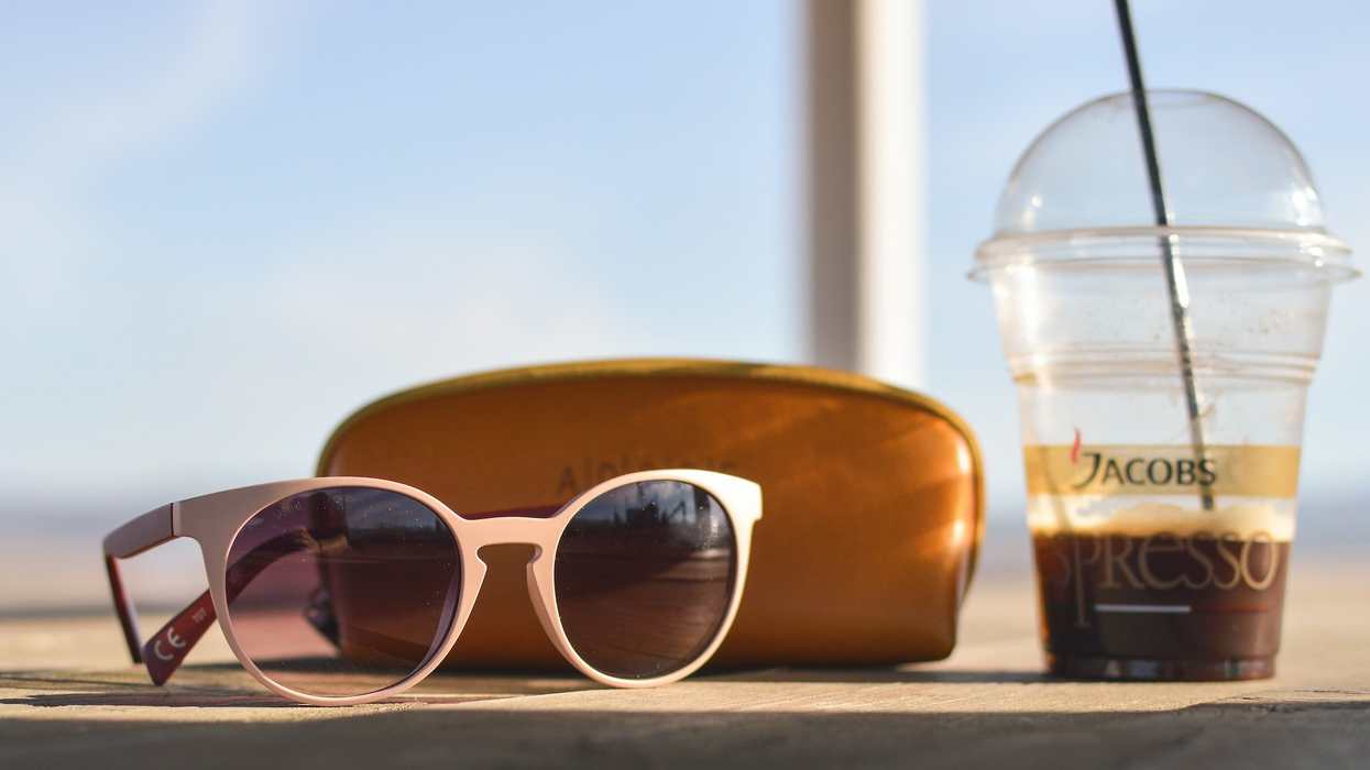 A pair of sunglasses, their case and an iced espresso coffee are placed on top of a counter
