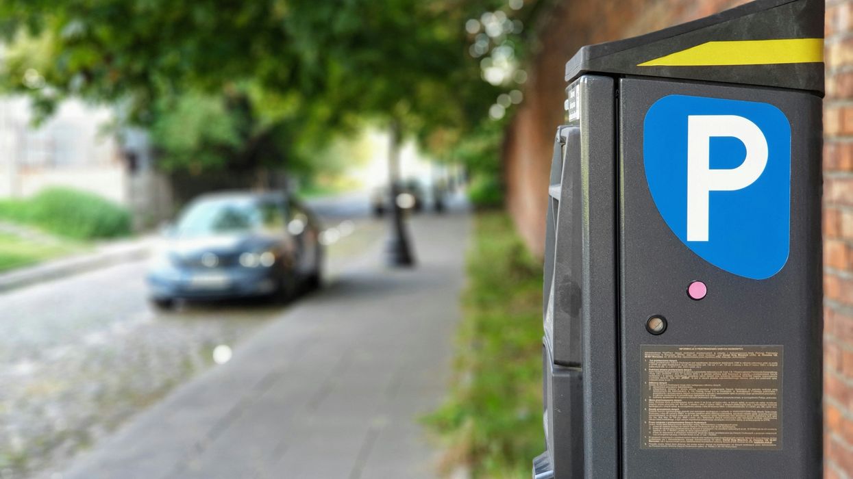 A parking payment machine with a car parallel parked in the background.