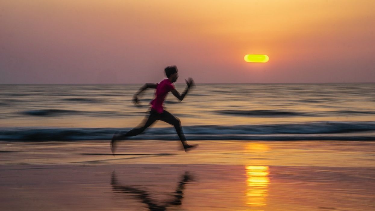 A person runs on a beach at sunset