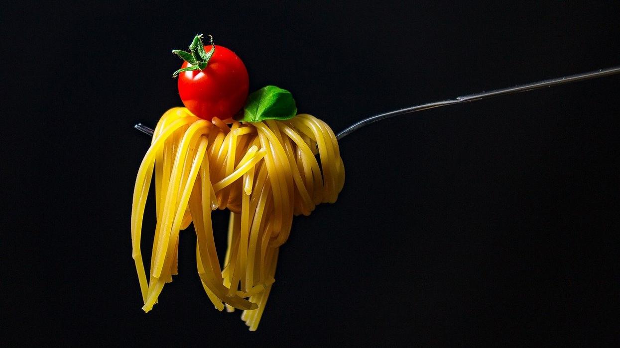 A photo of spaghetti, a tomato and a basil leaf on a fork