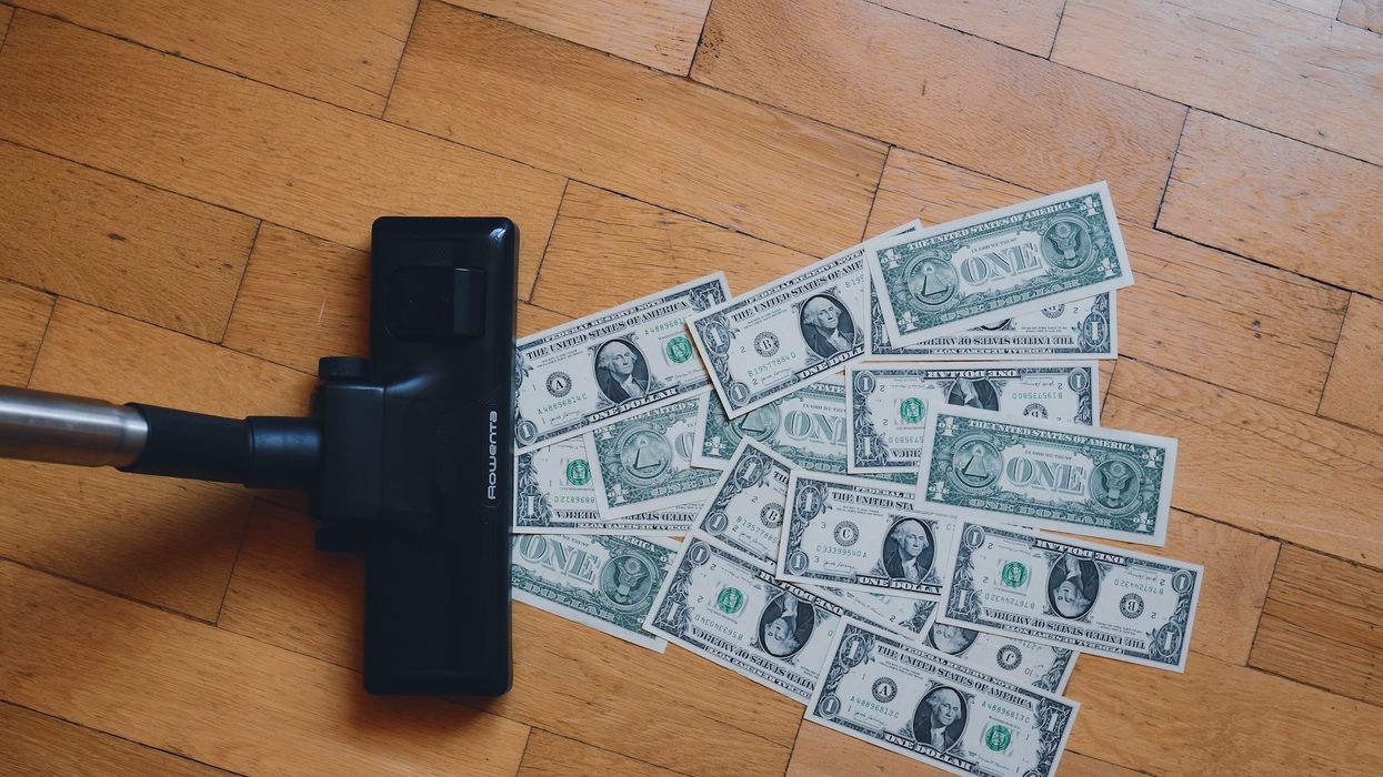 A pile of money is being vacuumed up from a wooden floor