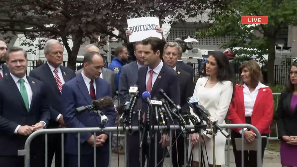 A protester holds a sign behind Republicans gathered outside Manhattan courthouse