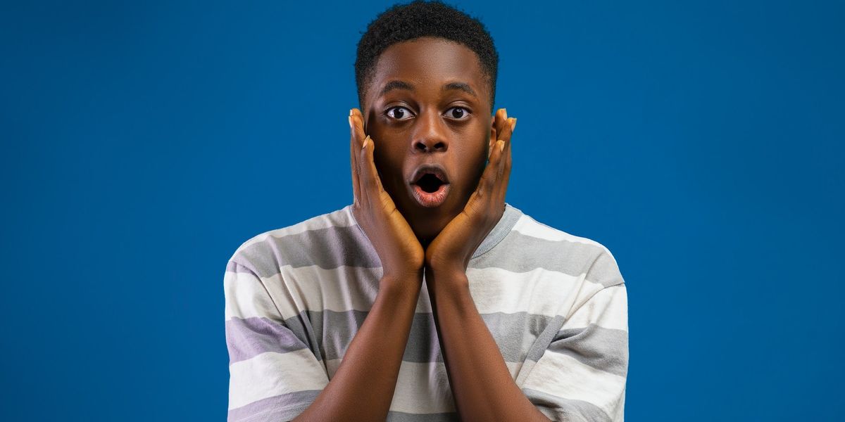 A shocked young man cups his face with his hands