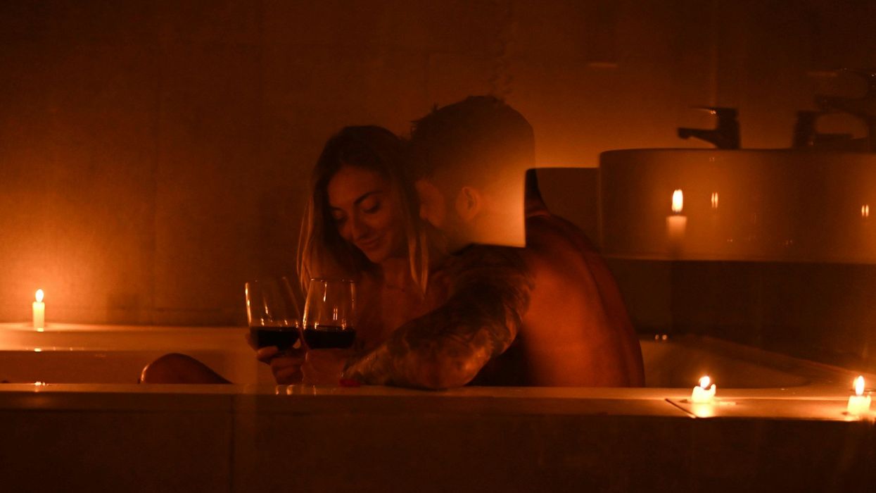 A shot, lit only by candle light, of a couple in a tub snuggling and sipping wine.