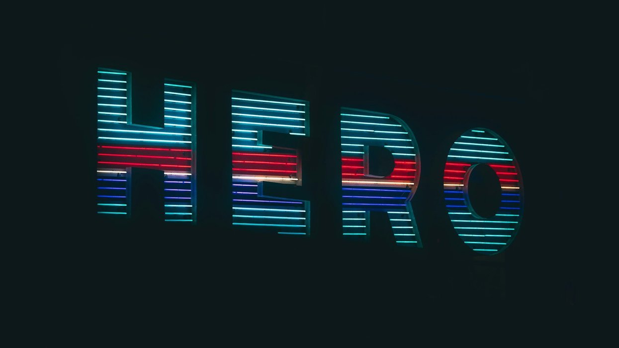 A shot of neon sign saying hero in capitol letters against a black background. The neon colors are red, white, dark blue and light blue.
