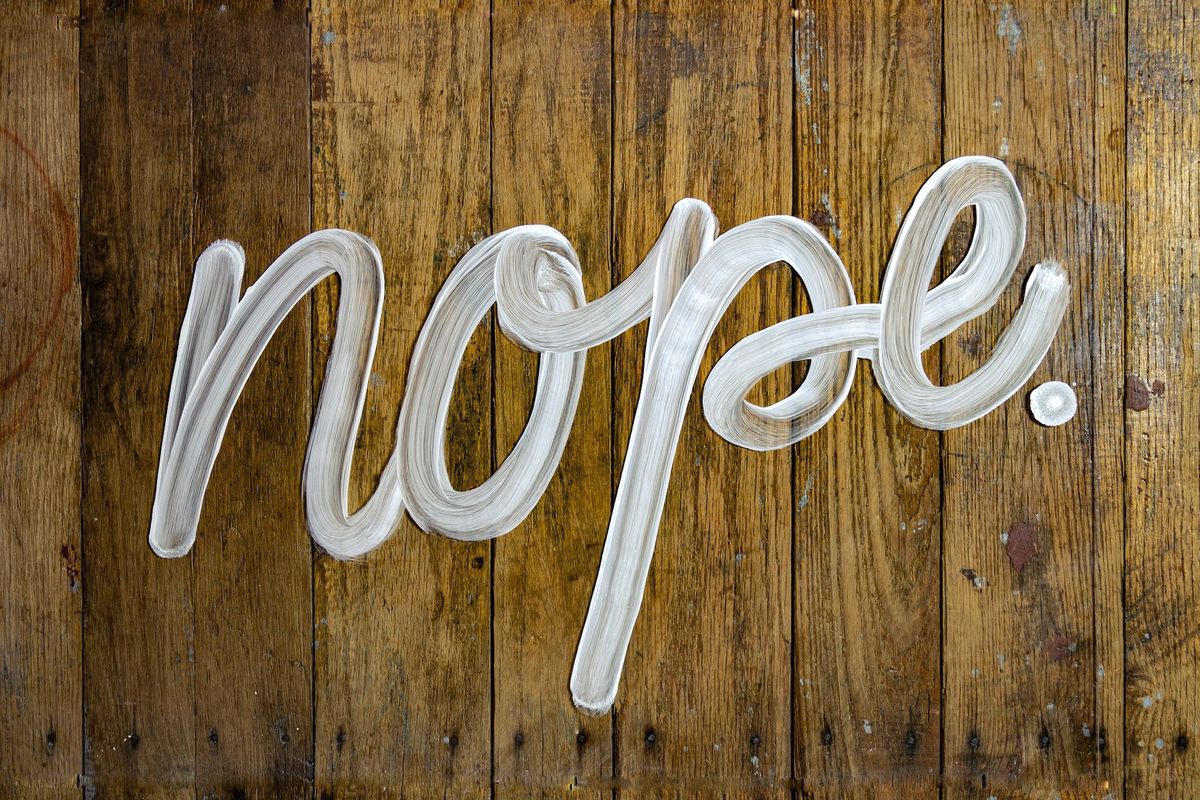 A sign saying "NOPE" written in white paint on a wooden wall 