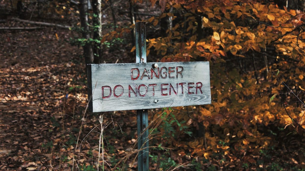A sign stating "DANGER. DO NOT ENTER" sits in a wooded area